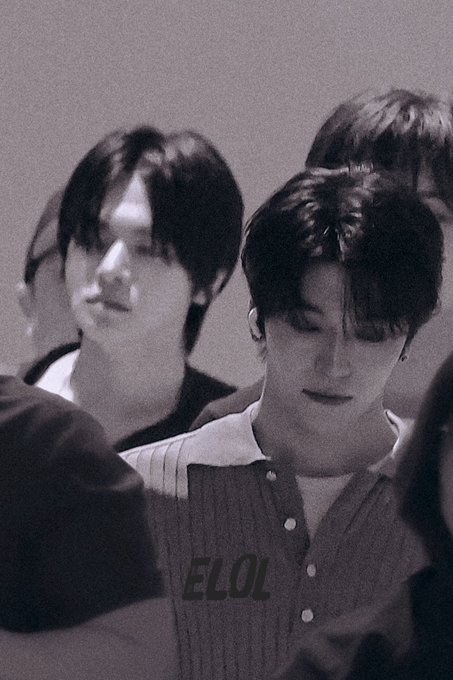 A grainy, black-and-white photo of two young men, likely K-pop idols, with dark hair looking downward; the image is watermarked with 'ELOL'.
