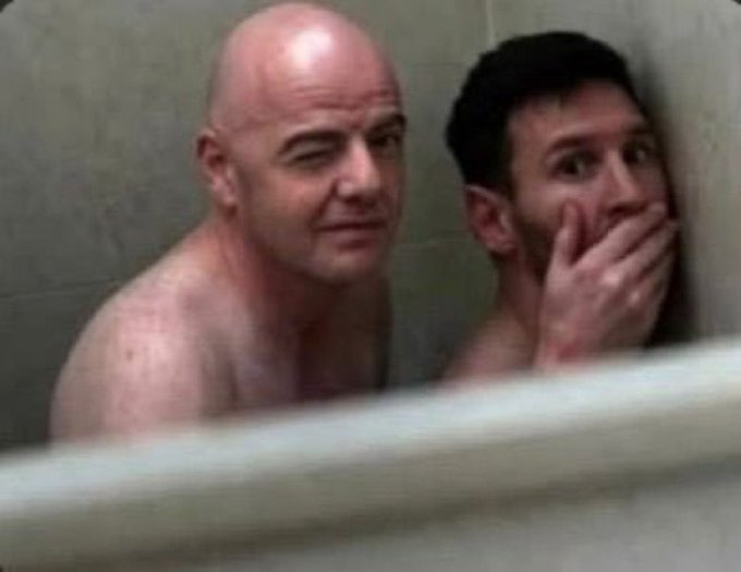 A blurry image showing two shirtless men in what appears to be a shower or bathroom setting, with one bald man looking toward a dark-haired man who has his hand over his mouth in a shocked expression.