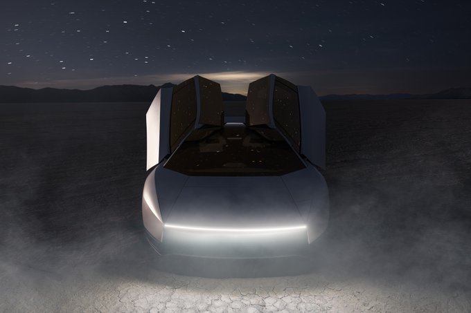 A futuristic silver car with upward-opening gull-wing doors sits on cracked ground at night, illuminated by its sleek headlights under a starry sky.