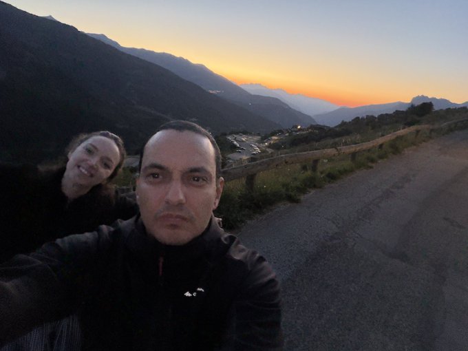A selfie of a couple with a mountainous landscape and sunset in the background.