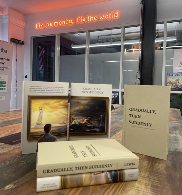 A display of copies of the book 'Gradually, Then Suddenly' by Ward Speed, with a neon sign reading 'Fix the money, Fix the world' in the background.