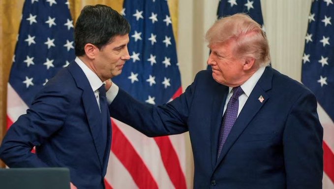 Two men in dark suits stand facing each other in front of American flags, with one man placing his hand on the other's shoulder in what appears to be a formal or congratulatory gesture. The image accompanies a post about the Federal Reserve, suggesting the men may be Donald Trump and a Federal Reserve official discussing monetary policy decisions.