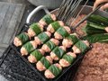 A tray of neatly wrapped meat rolls wrapped in green leaves, likely prepared for cooking, sits on an outdoor surface alongside green onions, illustrating the mother's quick and precise preparation skills highlighted in the post.