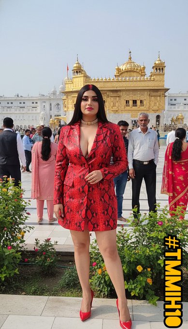 A woman in a red snakeskin-patterned dress posing in front of the Golden Temple, with other visitors and a garden in the background, tagged #TMMHI10.