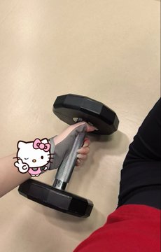 A first-person view of someone lifting a silver dumbbell with black weights, with a Hello Kitty sticker overlay.