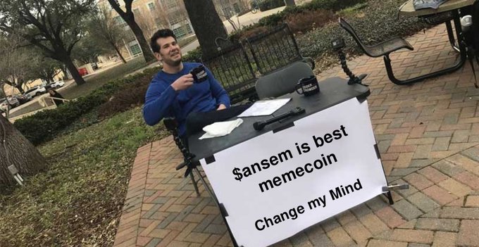 A man sitting at a table outdoors with a sign reading '$ansem is best memecoin - Change my Mind,' a parody of the classic Stephen Crowder meme format.