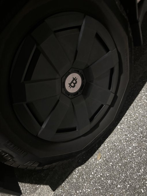 A close-up of a black car wheel featuring a Bitcoin logo on its center cap.
