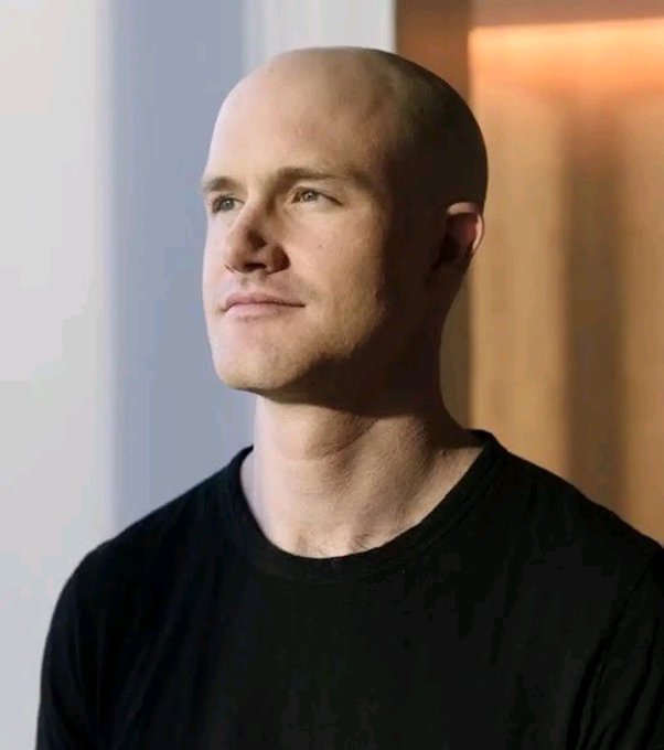 A portrait photo of a bald man wearing a black t-shirt, looking slightly upward against a softly lit background.