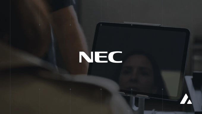 A cinematic frame showing a person viewing a screen with the text 'NEC' overlaid, with a reflection of a face visible on the monitor.