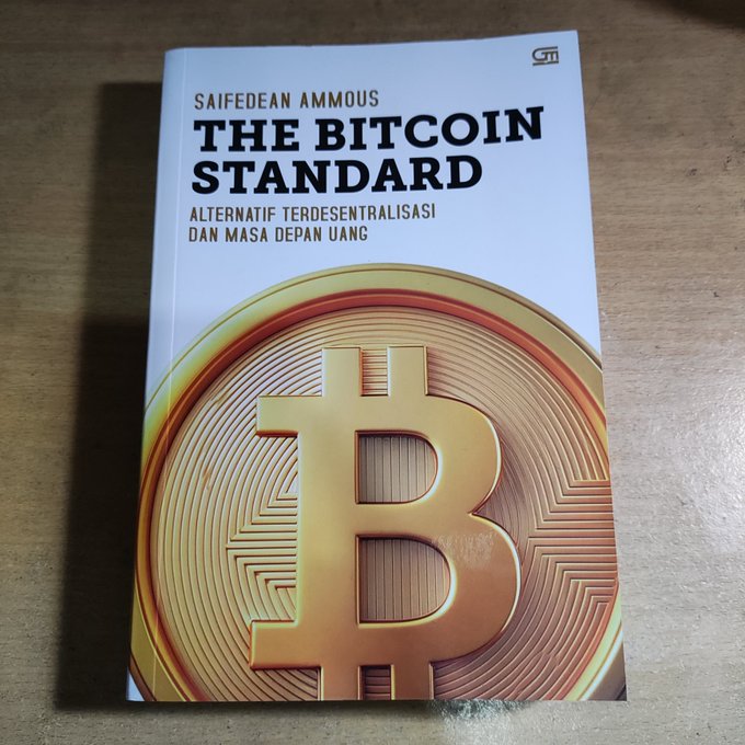 A book titled 'THE BITCOIN STANDARD' by Saifedean Ammous, with the Indonesian subtitle 'Alternatif Terdesentralisasi dan Masa Depan Uang,' features a large Bitcoin coin on the cover.