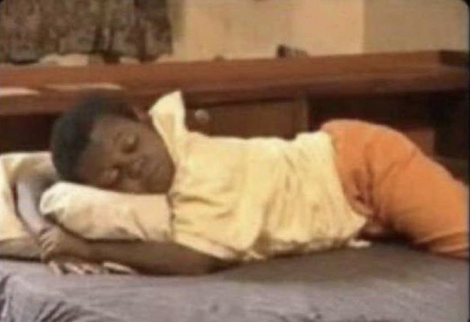 A vintage television still of a young child lying asleep on a bed with white sheets and orange pants.
