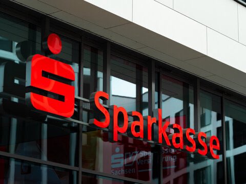 The exterior signage of a Sparkasse bank branch, with the red 'S' logo and 'Sparkasse' name displayed on a glass facade.