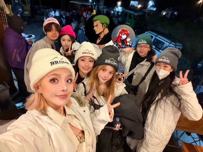 A group of people wearing "BROMO" beanies taking a selfie, with images of the anime characters Zoro and Nami superimposed over the background.