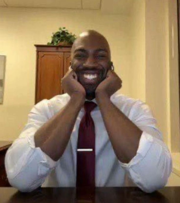 A smiling, bald Black man in a white dress shirt and burgundy tie sits at a table with both hands pressed against his cheeks in an expression of joyful excitement. The accompanying post "good news bnb maxi" suggests the image is a reaction meme conveying enthusiasm about positive news for a Binance Coin (BNB) supporter.