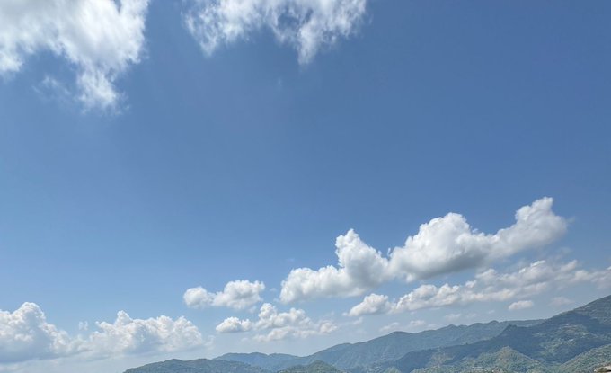 The image shows a beautiful view of a mountain range under a clear blue sky with white clouds. The mountains are covered in lush green trees, creating a picturesque scene. In the bottom right corner of the image, there is text that reads "Good morning everyone. operators been sleeping on this your idle machines are literally printing nothing while ai labs pay premium rates for compute they can' t find @quipnetwork flips that plug in, resell your excess capacity, earn without the complexity". The focus of the image seems to be on the stunning landscape and the captivating sky, rather than the text.