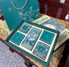 An open decorative green gift box displayed on a wooden table, with a matching gift bag visible in the background.