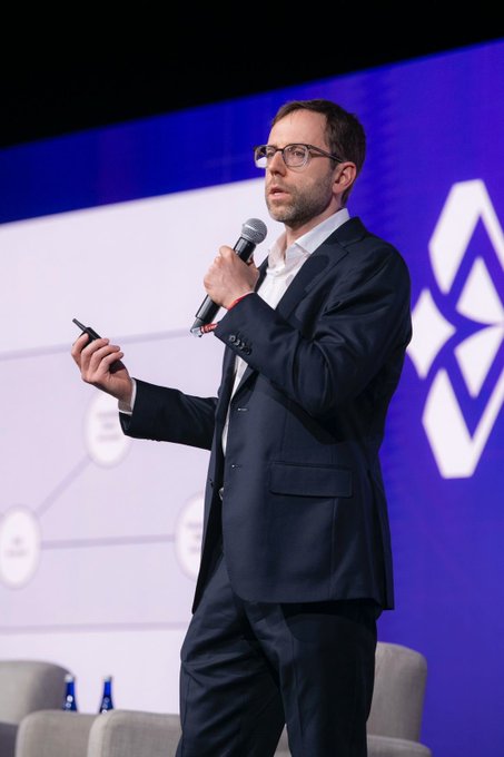 iced coffee and water bottles are displayed on a table, with a man in a suit holding a microphone against a blue backdrop featuring the IBM logo.