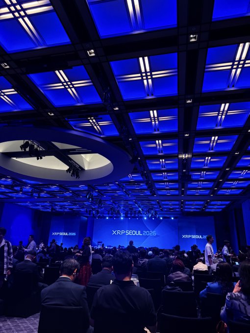 A large conference hall with blue lighting, displaying 'XRP SEOUL 2025' signage on the stage where attendees are seated facing forward.