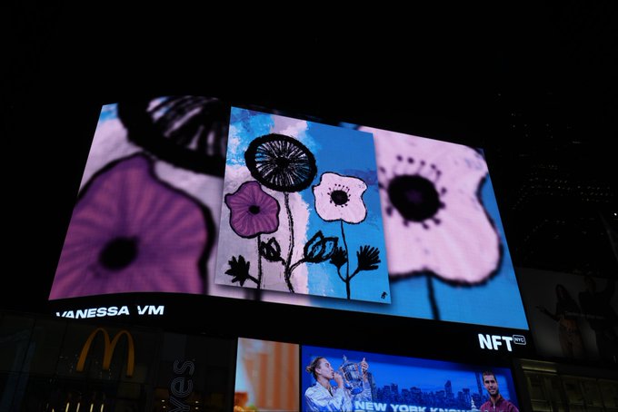 A large outdoor digital billboard displays artwork featuring stylized flowers in purple and pink tones against a blue background, with 'NFT' visible on the side.