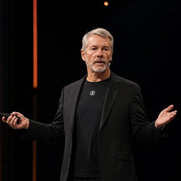 Michael Saylor, the executive chairman of MicroStrategy, speaks on stage while gesturing with his hands, illustrating his point about corporate Bitcoin adoption being "necessary and inevitable" for institutions.