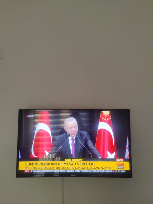 A television screen mounted on a beige wall broadcasting a CNN Türk news segment featuring Turkish President Erdoğan speaking at a podium with Turkish flags, with the chyron reading 'CUMHURBAŞKANI NE MESAJ VERECEK? ERDOĞAN BEŞTEPE'DEKİ KON TOPLANTISI SONRASI AÇIKLAMA YAPIYOR'.