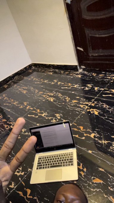 A person makes a peace sign while sitting on a marble floor with a laptop, with only the top of their head visible at the bottom of the frame.