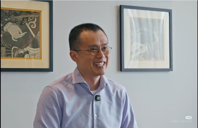 An interview shot of a smiling Asian man wearing glasses and a light purple button-down shirt, with framed artwork visible on the wall behind him and a 'Made in Indonesia' watermark in the corner.
