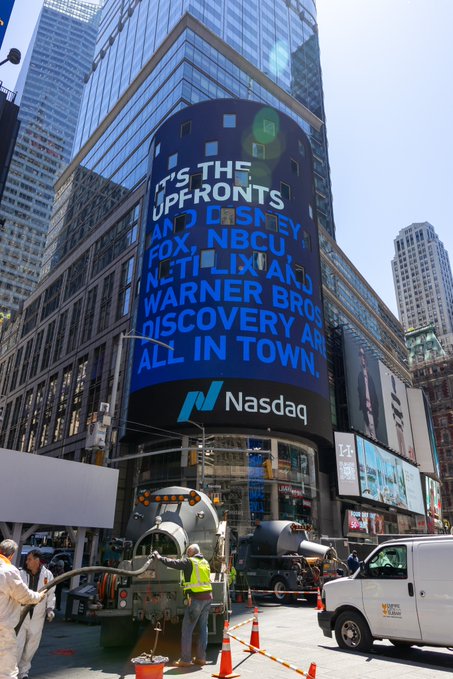The Nasdaq MarketSite billboard in Times Square displays "IT'S THE UPFRONTS AND DISNEY, FOX, NBCU, NETFLIX AND WARNER BROS DISCOVERY ARE ALL IN TOWN" in blue text, with workers in safety vests operating machinery on the street below.