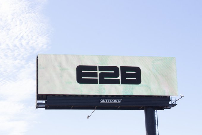 A billboard against a blue sky displays the text "E2B" with "OUTFRONT" branding visible below.