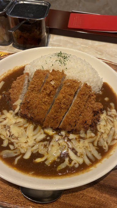 A bowl of katsu curry featuring a breaded and sliced cutlet over rice, covered in curry sauce and melted cheese.