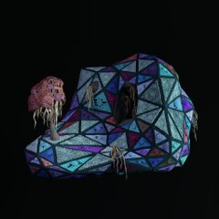 A dark, low-resolution image showing a geometric, multi-colored dome-like structure with small, skeletal figures hanging from it.