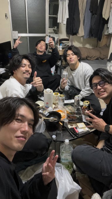 A group of five young men gather around a cluttered table filled with empty beer cans, sake bottles, and hot pot dishes in a small, cramped room. Visible text on a beer can reads "Clear Asahi," capturing a lively drinking session that humorously contrasts with the caption's lament about health and finances deteriorating due to alcohol and cigarettes, while still chasing XRP information.