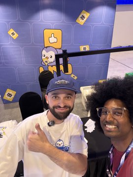 Two men smiling for a photo at what appears to be a convention or event, with one wearing a blue 'Pudgy Penguins' cap.