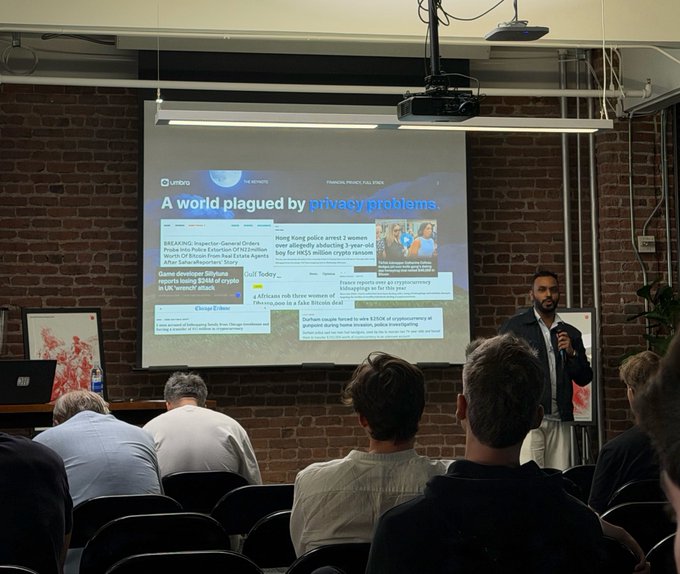 A man speaks to a seated audience while presenting a slide titled "A world plagued by privacy problems" showing various news headlines about crypto and security issues.