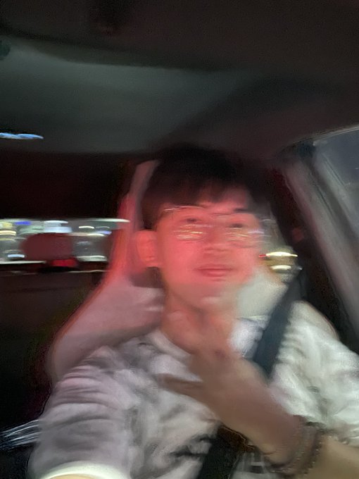 A blurry selfie of a young man wearing glasses inside a car, with city lights visible through the window, appears to be the "proof of life" photo accompanying the casual claim that he's still around and jokingly noting the rumored return of NFTs.
