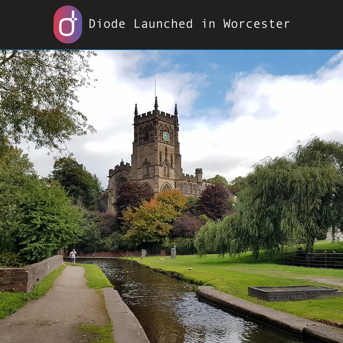 A promotional graphic featuring the text 'Diode Launched in Worcester' alongside the Diode logo, set above a scenic view of a historic stone church with a tall tower beside a tranquil canal lined with trees.