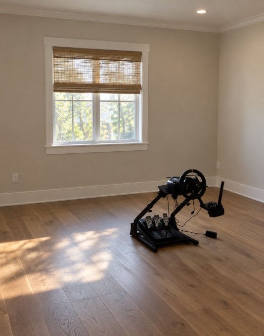A racing simulator setup sits alone on the hardwood floor of an otherwise empty room with a large window, awaiting its monitor and chair to complete the "rate my setup" experience.