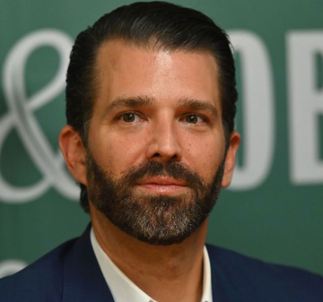 A man with dark hair and a beard, wearing a navy blazer, poses in front of a green backdrop featuring partial "OBE" lettering. The image relates to Donald Trump Jr., whose firm 1789 Capital is making a major investment in Polymarket.