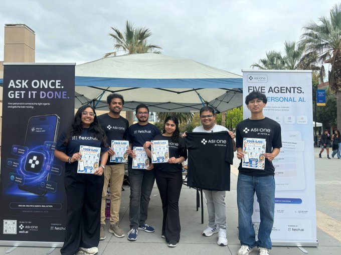 A group of six people posing outdoors at a promotional booth for 'ASI:ONE' featuring banners that read 'ASK ONCE. GET IT DONE.' and 'FIVE AGENTS. ONE PERSONAL AI.', with team members wearing branded shirts from ASI:ONE and fetch.ai.