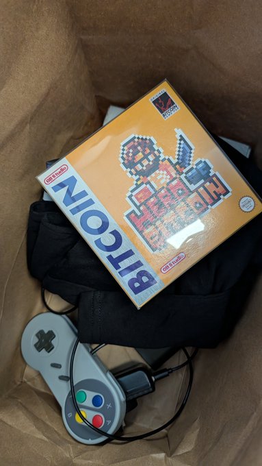 A Nintendo GameCube console with a controller sitting next to the original 'Super Mario Advance 4' game box on top of a black bag.