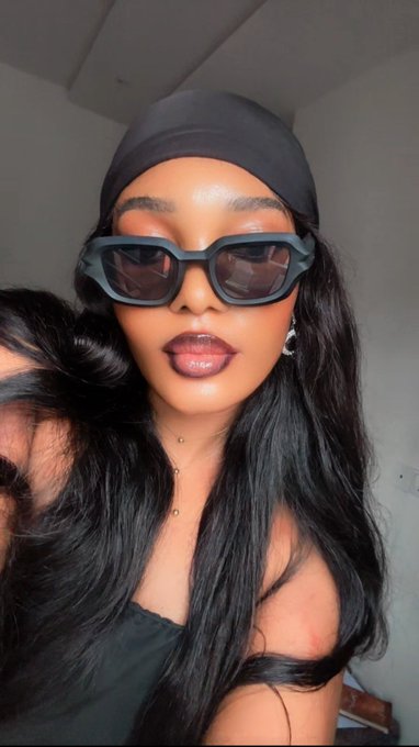 A stylish woman wearing dark sunglasses and a black headwrap poses for a selfie, with long flowing hair and glossy lips. The image complements the post's appeal to @blknoiz06 for a $6,000 $ANSEM allocation, showcasing the personal, confident branding of a small African KOL advocating for the crypto community.