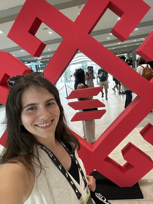 A smiling woman wearing sunglasses on her head and a lanyard with a "Mt. Serbia" badge poses for a selfie in front of a large red Solana Summit sculpture at the event. The image complements the post by visually showcasing her attendance at the Solana Summit Serbia, where she's enjoying the well-organized conference despite tired feet from exploring the thriving ecosystem.