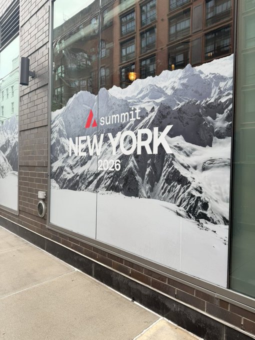 A street-level advertisement on a building window for 'summit NEW YORK 2026' featuring an image of snow-capped mountains.