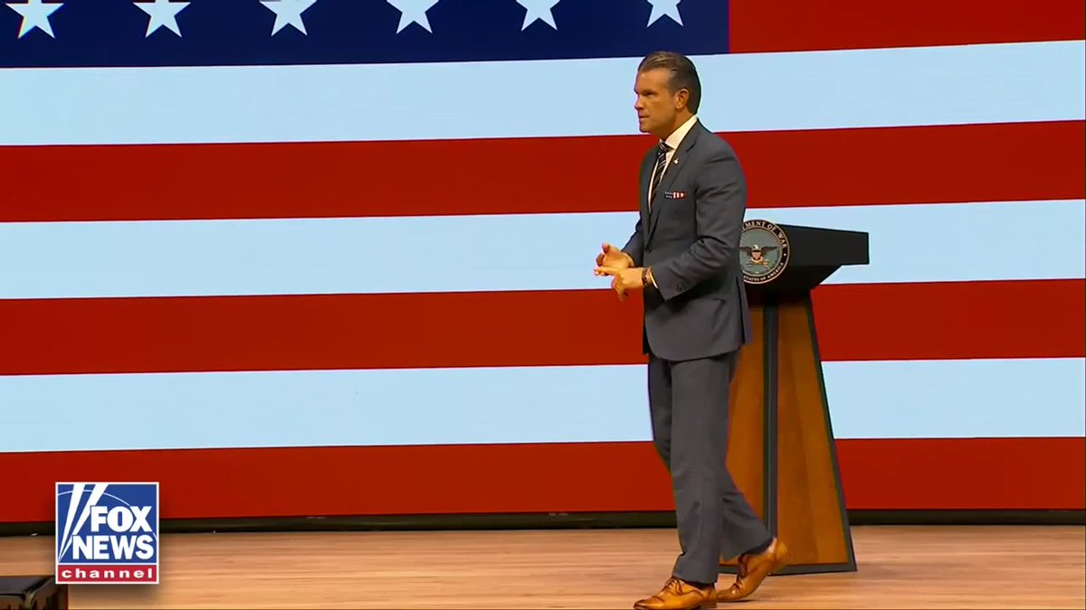 Fox News Channel broadcast showing a man in a dark suit standing on stage in front of an American flag backdrop next to a podium with a Department of Defense seal.