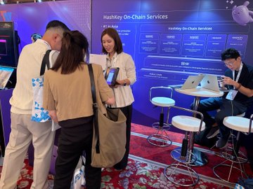 A photograph taken at a conference showing people gathered around a 'HashKey On-Chain Services' booth, with attendees looking at tablets and phones.