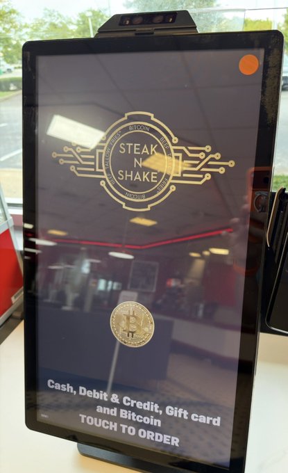 A 'Steak N Shake' digital ordering kiosk displaying the logo with circuit board design, a Bitcoin coin graphic, and text reading 'Cash, Debit & Credit, Gift card and Bitcoin - TOUCH TO ORDER'.