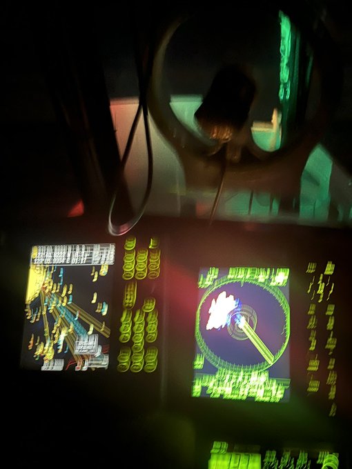 A view inside a dimly lit vehicle showing two bright digital screens displaying technical schematics and diagrams in green and yellow colors.