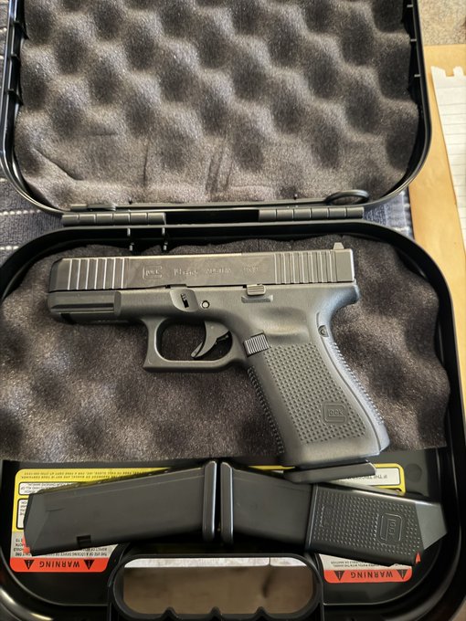 A new Gen 5 Glock handgun rests in its foam-padded carrying case alongside an extra magazine and a warning-labeled accessory, consistent with a freshly unboxed pistol.