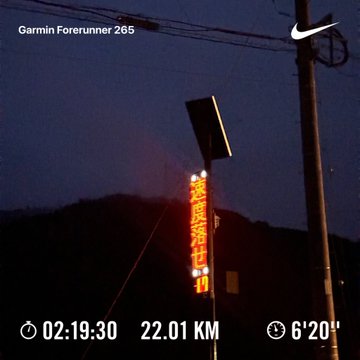 A low-light nighttime photo taken with a Garmin Forerunner 265, showing an illuminated street sign and utility pole, with stats overlay reading 02:19:30, 22.01 km, and 6'20" pace.