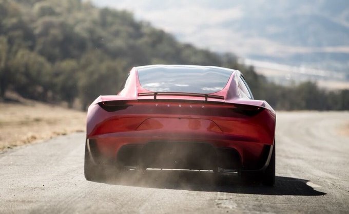 A red Tesla Roadster prototype speeds away on a dusty road, kicking up dust behind it as it showcases the sleek rear design and prominent Tesla lettering. The image previews the upcoming unveiling of the new Roadster on October 1, hinting at the performance and styling of the latest model.
